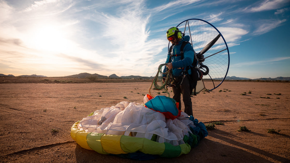 A paramotor pilot preparing for flight in the desert at sunset