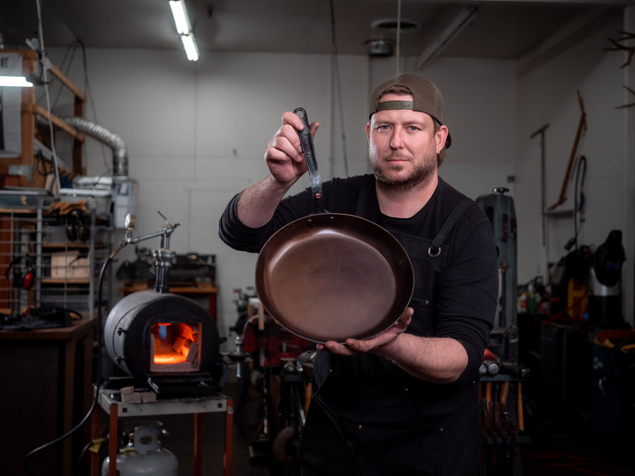 A blacksmith holding a handmade carbon steel skillet in his workshop