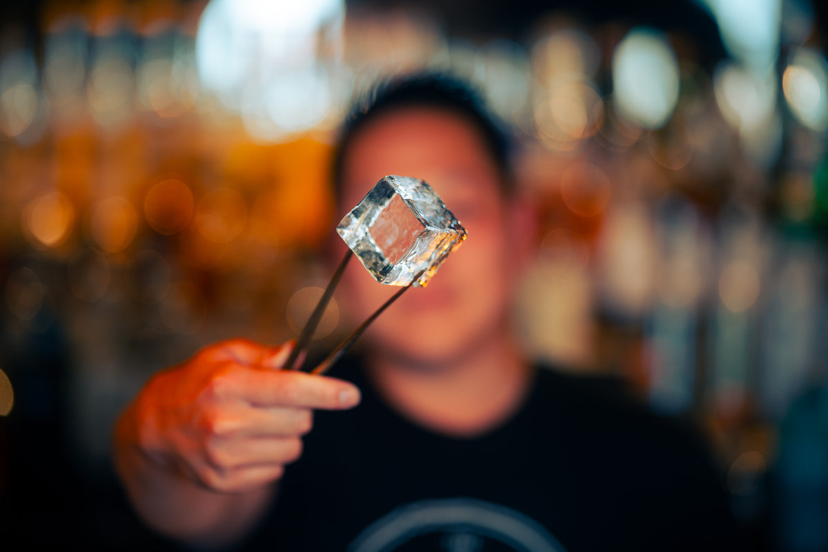 A bartender presenting a clear ice cube at the bar